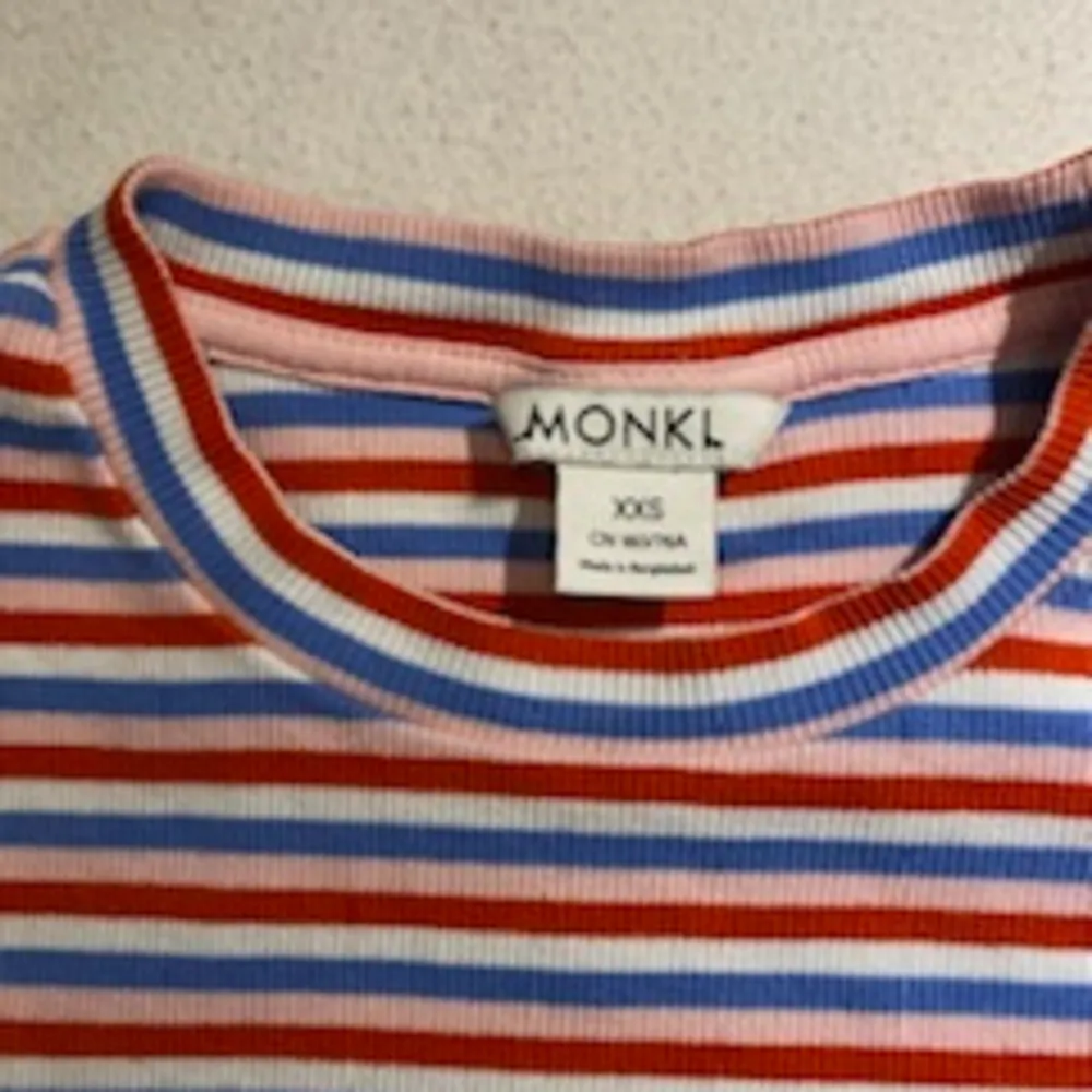 En randig t-shirt med färgerna vit, blå, rosa och röda. Den går ganska långt ner på magen, är storlek xxs och är från Monki.. T-shirts.