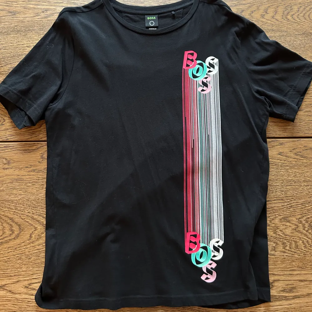 En svart Hugo boss t-shirt med färglatt motiv, som ger en ”3D-känsla”. Tröjan är sparsamt använd och i väldigt fin skick. Storlek Medium.. T-shirts.