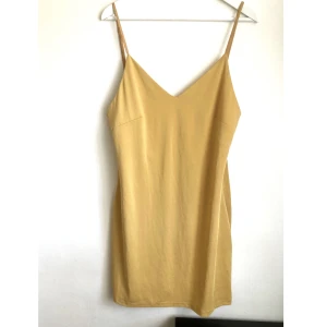 Senapsgul slip klänning, L 44/46, mini, y2k, minimalistisk, underklänning, mustard, v-ringad - Slipklänning i dämpad senapsgul färg. Elastiskt material, justerbara axelband (längd samt kan korsas). Finns slitage på axelbanden.  Mått i cm: bröstvidd 49; längd från axeln utan axelband inräknat 75.