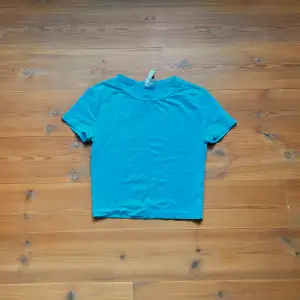 Kort, tajt t-shirt i en klar turkos färg. Fint skick och i princip helt oanvänd. 