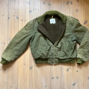 50/60-tals bomberjacka  - Riktigt gammal militär/bomberjacka med foder. Den har en boxy och kort silhuett, storlek L. Måttet på bilden är ungefärligt 