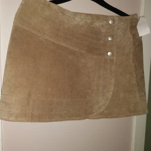 Kort kjol i mocka.. Läder  -  Stängs med tryckknappar, ca 34cm lår kort sandfärgad