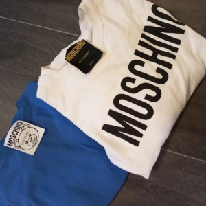 Moschino collegetröja och finstickad - Två tröjor i fint skick. Använda vid några få gånger. Hela och rena. Den vita är kritvit och endast tvättat en gång. Den blå aldrig tvättad bara prövad. Säljes i paket med både för 800 kr. Pris i butik för båda ligger på ca 4000kr.