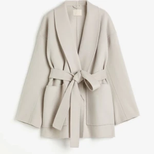 Ull kappa  - En kort kappa i ull med sjalkrage och avtagbart knytskärp i midjan. 