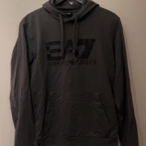 EA7 hoodie - Säljer en mörkgrå ea7 hoodie i väldigt bra skick, säljes då den är förliten. Strl small, kom privat för fler frågor och bilder!