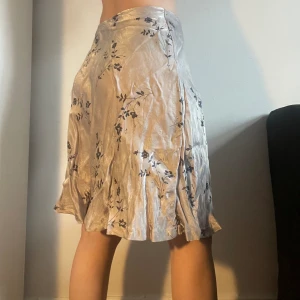 Blommig kjol i grått/blått - Midikjol i ett skimrigt gråblått tyg med blå blommor på. Den är insydd för att passa storlek s, går till knäna på mig som är 165 cm. Möts på söder eller postar. Skriv helst innan ni trycker köp nu då jag är borta en del i sommar. 