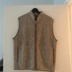 J.Lindeberg tiger brown väst  - En snygg och bekväm väst i en mjuk och varm färg. Västen har en dragkedja framtill och två fickor på sidorna. Den är perfekt för att hålla dig varm under kallare dagar.