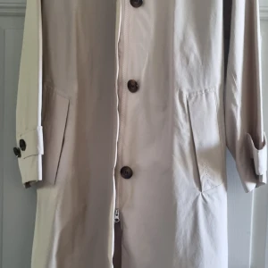 Trenchcoat Barbour - Ny benvit trenchcoat från Barbour i strl 36 men rymlig, passar upp till 40. Vind och vattentät med grönrutigt foder. Långt skärp som är fäst i ryggen med knapp. Många exklusiva detaljer. Kan skicka fler bilder. Nypris 4200 kr.