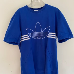Blå adidas t shirt - En adidas tröja med tre streck som går runt tröjan och märket i mitten. Storlek s men stor i modellen, välbehållen färg. Det enda som stör är lappen i nacken som kan sticka ut lite. Skriv om frågor!