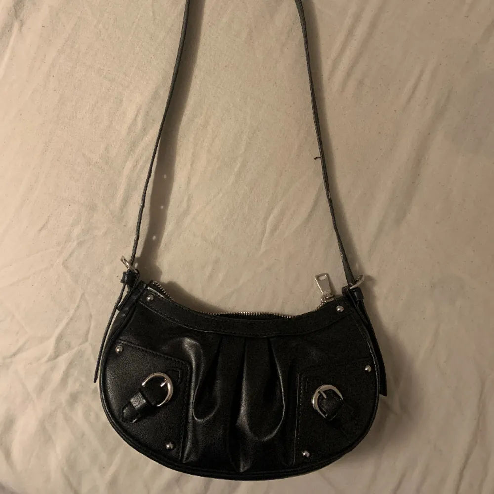En svart handväska med silver detaljer som man kan ändra längd på. . Accessoarer.