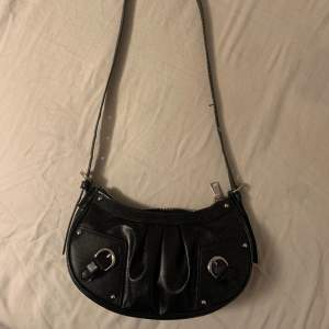 En svart handväska med silver detaljer som man kan ändra längd på. 