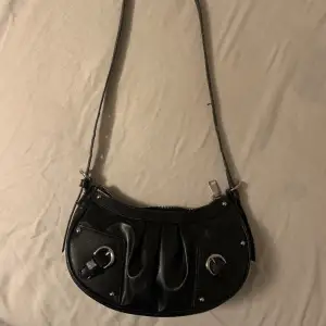 En svart handväska med silver detaljer som man kan ändra längd på. 