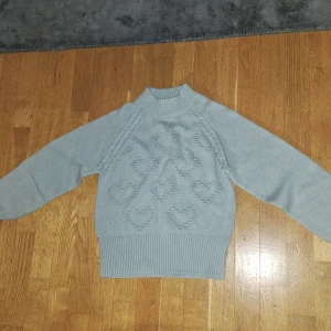 Blå tjocktröja med hjärtan - Den är egentligen pastelblå men den ser gråare ut i kameran. Baksidan och framsidan är likadan. Tajta delen runt halsen och armarna går att stretcha ut. Har bara använt den en gång, det var när jag provade den. Jag tyckte att den inte passade
