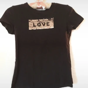 T-skirt med paljetter  - Svart Basic T-skirt med paljetter som man kan vända så det blir olika färger, svart eller grå i texten LOVE. Inga anmärkningar. Storleken är 146/152.