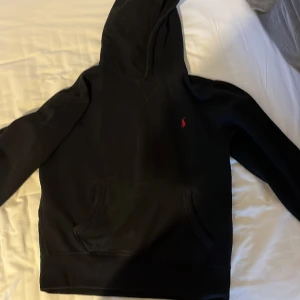 Polo Ralph lauren hoodie - Säljer denna sjukt snygga polo Ralph lauren hoodie, Hoodien är svart med en röd logga, tröjan har blivit för liten för så de är därför jag säljer den, tröjan är fortfarande i riktigt bra skick. Säljer i väldigt bra pris Skick 9/10
