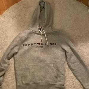 Tommy Hilfiger Hoddie - En hoddie som är använd rätt så många gånger. Fortfarande i ett bra skick. Skriv om du vill ha fler bilder på hur den sitter och den ser ut.