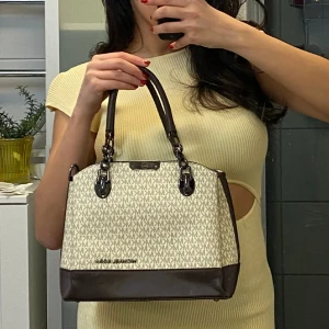 Michael kors väska - En Michael kors väska i färgen beige och brun. En medium väska som har ganska många fickor. Saknar den långa bandet