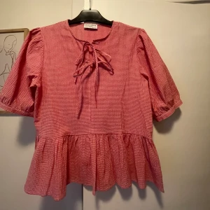 Blus/peplumtopp - Rutig blus med en kort puffärm och knytstängning på framsidan. Nypris 349kr, slutsåld. Skriv för fler bilder:)