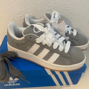 NYA Adidas Campus 00s j storlek 36 - Färg: Grå (Grey Three) Ingår både vita och gråa skosnören.  Nya och oanvända. Ligger kvar i kartong. Det finns dock en pytteliten fläck på en sko som är någon typ av gummibeläggning (troligtvis från tillverkningen?) Se bild. 