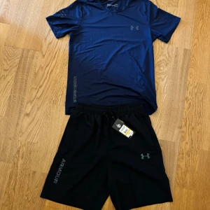 Under Armour Set - Helt ny under armour set till sommaren med lysande detaljer. Toppen är mörk blå och shortsen har en liten blå ton i färgen. Toppen är i storlek M och shortsen i storlek L.  De är normal fitted. Priset är för både tröjan och shortsen. 