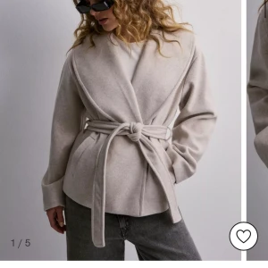 Oanvänd Ljus beige kort kappa med band - Helt oanvänd ljus beige kort kappa ifrån Nelly i strl M. Säljer då jag aldrig använt den då färgen ej passar mig. Ord pris 699  kr. Säljer för 350 kr då den är helt oanvänd.