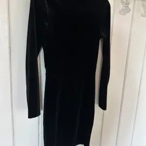 Långärmad svart klänning i sammets liknande tyg. Öppen i ryggen och perfekt för fest.