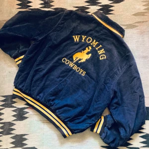 Vintage varsity manchester retro bomber jacka cowboy rodeo western  - Superfräck urblekt brun manchester varsity bomberjacka med gula detaljer, broderi på ryggen och gula tryckknappar.  Gult foder.  Bra vintage skick.   Längd 69cm Bredd 69cm Axel till axel 53cm Ärmlängd 51cm