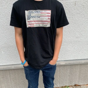 Ralph lauren t shirt🇺🇸 - Säljer denna Ralph lauren T-shirt med amerikanska flaggan🇺🇸 på. Tröjan kan se sliten ut men designen ska se ut såhär. Storlek M  han på bilden är 168cm. Men passar om man är upp till 175-185cm lång