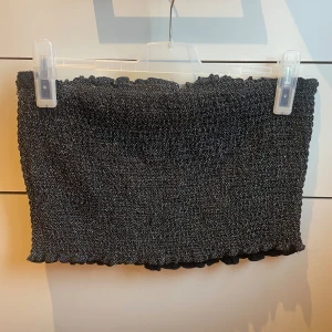 Glittrig tubtopp - OANVÄND (!!) Svart glittrig tubtopp från BikBok med resår/gummiband.  Bekvämt och lätt material.  Inköpt för 9månader sedan, på BikBok. 