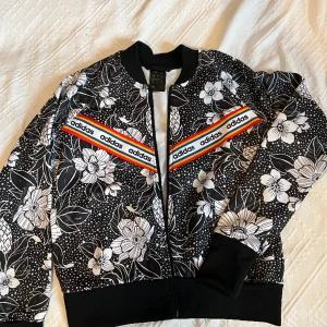 Adidas bomberjacka  - Använd 1 gång, som ny Liknar "Adidas Originals Farm Floral Placement Jacket" som kostar 800kr  Strl 164 men är oversized, passar S Säljer för jag aldrig använder den.  Kan mötas upp i Finspång/Norrköping eller skicka, köparen står för frakten :)