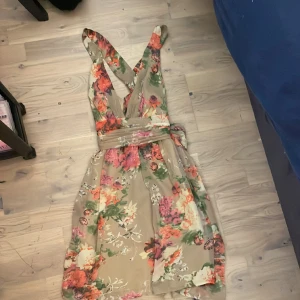 En beige blommig klännig - En beige blommig klännig som aldrig kommit till användning vilket betyder att den inte är använd. Prislappen finns på klänningen.