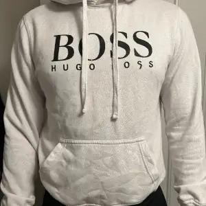 Vit Hugo Boss hoodie med svart tryck på bröstet. Tröjan är i gott skick! Ordinarie pris: 1500kr