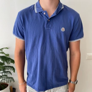Moncler Piké - Säljer nu en riktigt fräsch moncler piké. Pikén är storlek XL men passar L. Tröjan är i bra skick utan några skador eller liknande endast lite slitage i kragen (se bilder) hör av er vid frågor eller funderingar. 