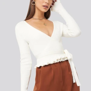 Blus - Blusen har en omvirad design med ett knytbart band vid midjan, en v-ringning, långa ärmar med en fransig detalj i nederkant och en mjuk stickning.  Naturvit färg. Går inte längre att köpa. Inga skador eller skavanker. Använd endast 1 gång.