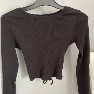 Svart lång armad tröja med öppen rygg - Denna fina svarta tröjan med detaljer på ryggen är en perfekt sommar tröja, som passar dig som gillar toppar. Toppen är i bra skick och använd några gånger! Inga skador på sig och är köpt från new yorker. 