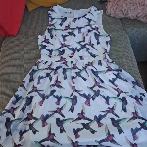 Vit ärmlös klänning med fågelmönster - En vit ärmlös klänning från only med ett färgglatt fågelmönster. Klänningen har en rund hals och en lätt utställd kjol. oanvänd. 100% ny . 