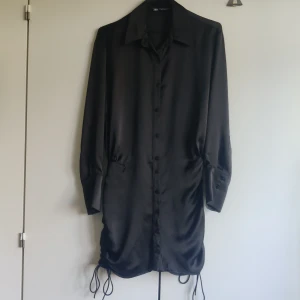 Sidenklänning - Svart klänning från Zara i storlek xs. Lite oversized upptill med tightare kjol med dragsko i sidan. Knyts nedtill. Har några mindre tråddragningar på ett par ställen (se bild) men ingenting man tänker på