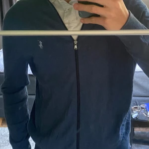 Blå tröja med dragkedja från Ralph Lauren - En blå tröja med dragkedja från Ralph Lauren. Tröjan har en broderad logotyp på bröstet och långa ärmar. jag är 1,84. köptes i vår använd 5 gånger typ.