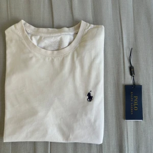 Vit t-shirt från Polo Ralph Lauren - En klassisk vit t-shirt från Polo Ralph Lauren med korta ärmar och rund halsringning. T-shirten är i fint skick, med en liten fläck på ryggen som inte syns vid använding. Skit snygg för sommarn, och passar med allt.  Inköpt på CareOfCarl för 1199, och säljs för 599. . Vid frågor kontakta gärna. Vi hörs i DM!