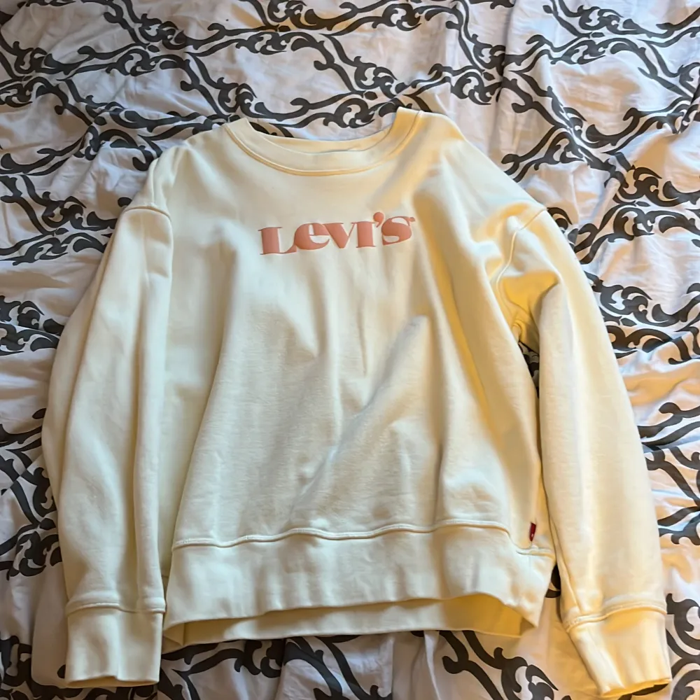 En vit sweatshirt från Levi's med rosa logotyp på framsidan. Tröjan har långa ärmar och ribbstickade muddar vid ärmslut och nederkant.. Tröjor & Koftor.