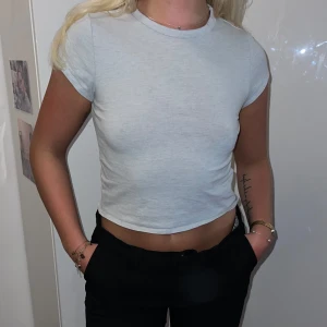 Vit croppad t-shirt från Gina Tricot - Säljer en vit croppad t-shirt. Den är kortärmad och har en tight passform. Perfekt för sommaren eller som en basplagg i garderoben. Använd men i bra skick.