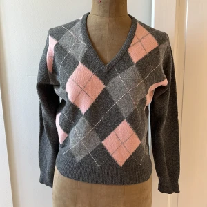 Grå och rosa argyle-mönstrad tröja från Pringle - Säljer en superfin grå tröja från Pringle med ett klassiskt argyle-mönster i rosa och grått på framsidan. Tröjan är gjord av 100% lammull och är riktigt mjuk och skön. Den har en v-ringad hals och långa ärmar. Perfekt för höst och vinter! 🩶🩷