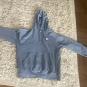 Grå hoodie från Nike - Säljer en blå hoodie från Nike i storlek XS. Den är supermjuk och bekväm, perfekt för kyliga dagar. Hoodien har en stor ficka på magen och en justerbar huva. Den är i bra skick och redo för en ny ägare!