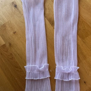 Ljusrosa extraarmar med spetsdetaljer - Säljer ett par supergulliga ljuslila extraarmar med fina spetsdetaljer. extraarmarna är ribbade och har en söt volangkant upptill. Perfekta för att ge en extra touch till din outfit! 💖jag har den i svart färg oxå 