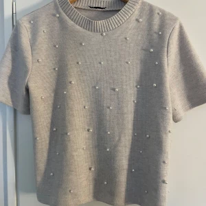 Grå stickad tröja från Zara - Säljer en superfin grå stickad tröja från Zara. Den har korta ärmar och är dekorerad med små pärlor över hela framsidan. Perfekt för både vardag och fest! Tröjan är i storlek L och är i mycket bra skick, liten i storleken så den passar S/M Passar perfekt till höst- och vårsäsongen. 🌟