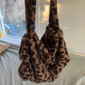 Leopardmönstrad axelväska i pälsimitation - Säljer en supercool leopardmönstrad axelväska i mjuk pälsimitation. Väskan har en bred axelrem och är perfekt för att ge din outfit en extra touch. Den är rymlig och passar både till vardags och fest. 🐆✨