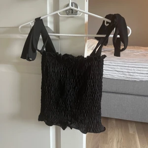 Svart ribbad linnetopp med knytband - Säljer en snygg svart ribbad linnetopp med knytband på axlarna från H&M. Toppen är ärmlös och har en tight passform. Toppen är helt oanvänd då den ej passade när jag fick den! Perfekt för sommaren eller en festkväll!  🖤