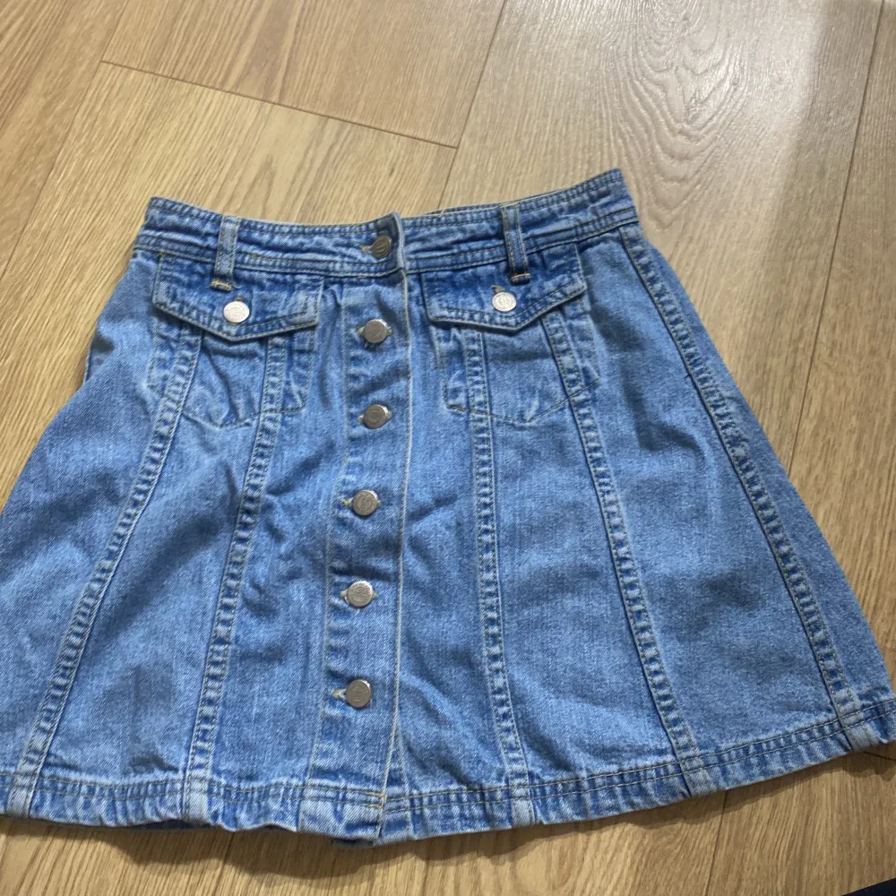 Säljer en superfin jeanskjol från Jeans for the Riot Girls. Den är i en klassisk blå jeansfärg och har en rad med knappar framtill. Kjolen har också två fickor med knappar på framsidan, vilket ger den en cool och avslappnad look. Perfekt för både vardag och fest! 🥳. Kjolar.