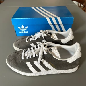 Gråa Adidas Gazelle  - Säljer nu mina gråa Adidas Gazelle-skor. Knappt använda, bara lite smuts som hur lätt som helst går att tvätta bort. Nypris 1299 kr. Box och gråa snören medföljer såklart, pris går att diskutera!