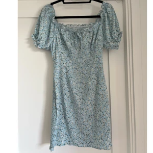 Blå blommig klönning - Ljusblå klänning med vita blommor, går att ha som offshoulder eller med armarna uppåt. Se detaljer på bilderna. Helt oanvänd 